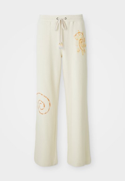 Pantaloni largi din tricot crem cu talie ajustabilă, grafică solară pe șoldul drept și design cu text spiralat portocaliu pe coapsa stângă.