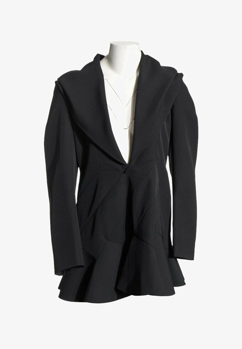 Blazer noir cintré avec larges revers, manches longues et ourlet évasé, présenté sur un buste de mannequin blanc.