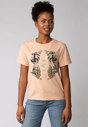 Licht perzikkleurig katoenen T-shirt met een bloemenpatroon in groene, gele en zachte roze tinten, met een ronde halslijn en korte mouwen.