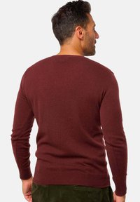 Burgunderfarbener Strickpullover mit rundem Ausschnitt, langen Ärmeln und gerippten Bündchen, der eine glatte Textur und einen figurbetonten Schnitt aufweist.
