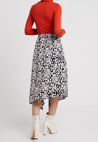 Červený top s dlouhým rukávem spárovaný s černou midi sukní s růžovým a bílým květinovým vzorem. Bílá kotníková obuv dotváří celý outfit.