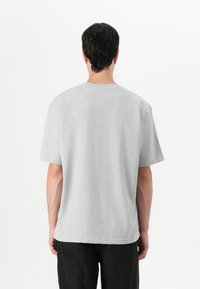 Tricou gri cu mânecă scurtă și guler rotund. Materialul pare a fi un amestec de bumbac. Linii curate, textură moale și croială lejeră. Vizualizare din spate.