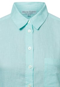 Light blue linen shirt with a point collar, front buttons, and a single chest pocket. Features a subtle texture and relaxed design.