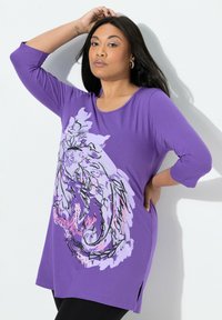 Fioletowa tunika z rękawami o długości do łokcia. Posiada duży kwiatowy motyw w kolorze różowym i czarnym. Boczne rozcięcia i miękki, lekki materiał.