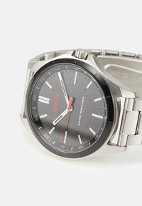 Reloj de acero inoxidable con esfera negra, detalles rojos y marcadores de hora plateados. Presenta un diseño resistente al agua y una pulsera de metal con eslabones.