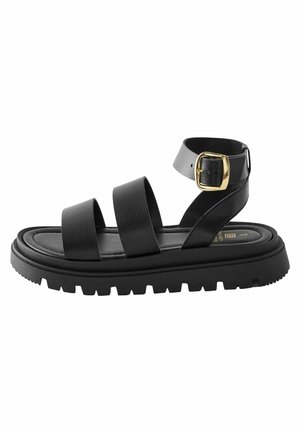 Sandale en cuir noir avec trois brides, semelle épaisse crantée et bride de cheville avec boucle dorée.