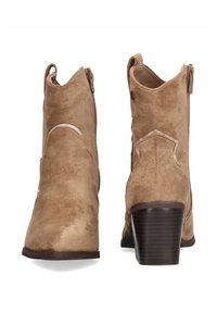Botines de ante en color beige con punta afilada, cierre con cremallera en la parte trasera y acentos curvados. Presentan un tacón apilado y una suela texturizada.