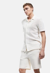Camicia bianca a maniche corte con bottoni, caratterizzata da un motivo ondulato testurizzato e pantaloni corti abbinati, realizzati in un tessuto traspirante.