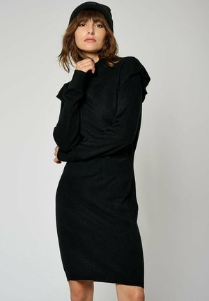 Robe pull noire avec des détails froncés aux épaules, manches longues et une silhouette ajustée. Fabriquée dans un tissu doux et texturé, longueur genou.
