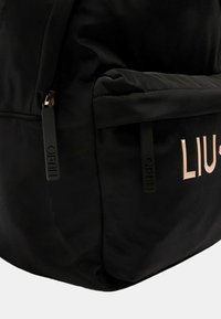 Zaino in tessuto nero con una texture liscia e morbida, caratterizzato da un logo rose gold prominente e zip nere per un design minimalista.
