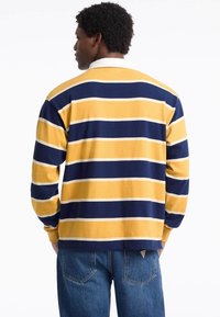 Long-sleeve, striped polo shirt in yellow and navy blue, with white stripes. Features a white collar and ribbed cuffs. Soft, textured fabric.