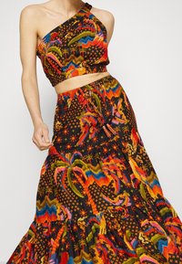 To-delt outfit bestående af en en-skulder crop top og en lang nederdel. Lavet af struktureret stof med et farverigt abstrakt mønster på en sort bund.