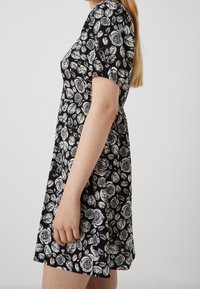 Černé šaty s bílou potiskem růží a listů, krátké nabírané rukávy, přiléhavý korzet a rozšířená sukně. Měkká látka s hladkým povrchem.