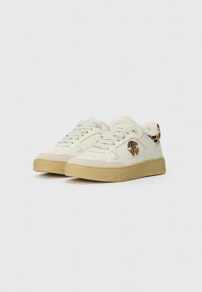 Pair of off-white low-top sneakers with beige soles, white laces, leopard print heel collar, and gold decorative emblem on sides.