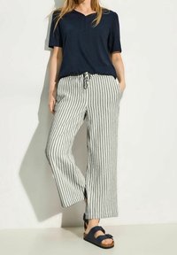 Navy short-sleeve top with a placket, paired with wide-legged black and white striped pants and dark sandals with ankle straps.