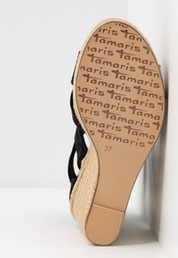 Sandale compensée noire avec une semelle intermédiaire en jute tressé et une semelle en caoutchouc, présentant un motif répétitif du nom de la marque sur la semelle extérieure. Taille 37.