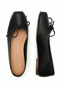 Zapatos planos de cuero negro con punta cuadrada y un acento de lazo. Exterior suave con una plantilla de color marrón claro y un bajo tacón de madera.