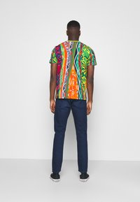 Kortärmad, flerfärgad t-shirt med en livlig abstrakt design, kombinerad med mörkblå jeans och svarta sneakers.