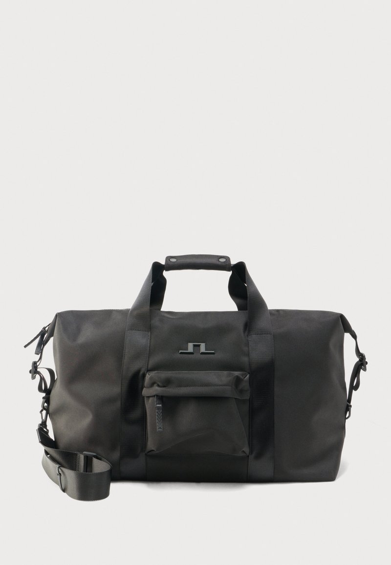 Μαύρη τσάντα duffel με διπλές λαβές, ρυθμιζόμενο ιμάντα ώμου, μπροστινή τσέπη με φερμουάρ και μινιμαλιστικό λογότυπο σε απλό φόντο.