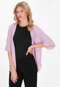 Cardigan lavorato a maglia di un leggero colore viola con un motivo testurizzato, con apertura frontale e maniche arricciate, indossato sopra un top aderente nero e pantaloni neri.