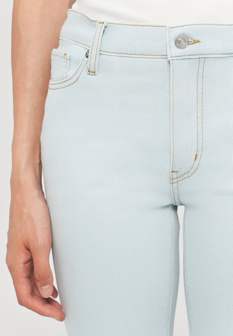 Hellblaue Jeans aus Denim mit glatter Textur, ausgestattet mit einem Reißverschluss, einem Knopfverschluss sowie gelben Nähten an Taschen und Nähten.