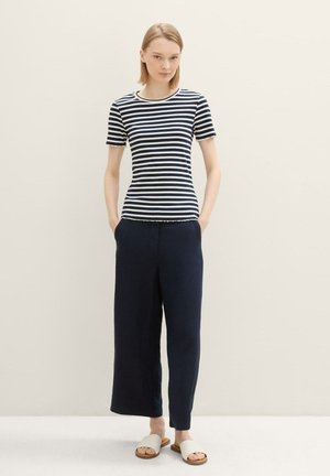Top corto a righe navy e bianche in cotone a maniche corte, abbinato a pantaloni larghi navy. Sandali leggeri e piatti completano l'outfit.