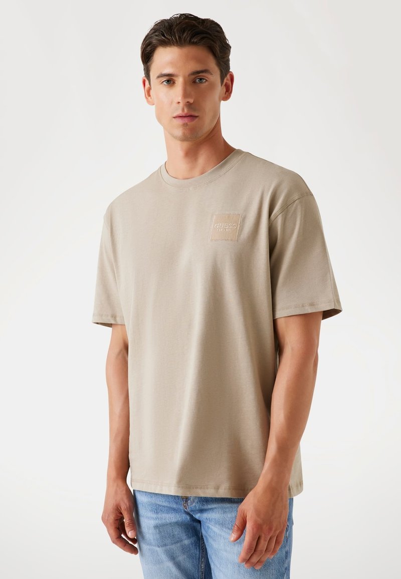 Beige bomulds t-shirt med rund hals, korte ærmer og et lille firkantet mærke med brandnavnet. Glat tekstur, afslappet pasform.