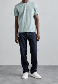 Světle zelené texturované tričko s krátkým rukávem v kombinaci s tmavě modrými džíny rovného střihu, doplněné bílými teniskami. Jednoduchý design, ležérní střih.