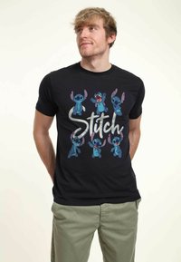 Black cotton t-shirt featuring multiple Stitch character prints in blue and pink, with "Stitch" text in metallic silver. Short sleeves.
