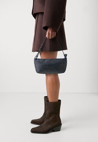 Marinblå handväska med rektangulär form, som har en strukturerad yta och ett kort svart handtag. Bärs tillsammans med bruna mocka ankelboots.