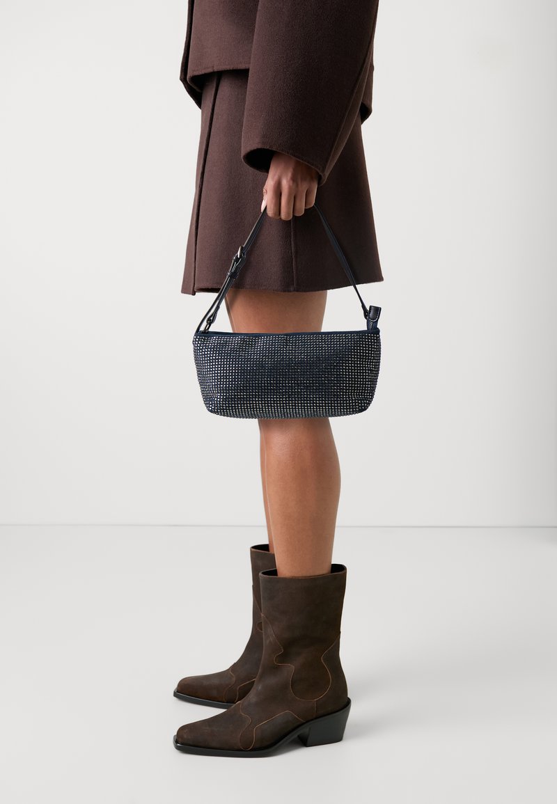 Marinblå handväska med rektangulär form, som har en strukturerad yta och ett kort svart handtag. Bärs tillsammans med bruna mocka ankelboots.