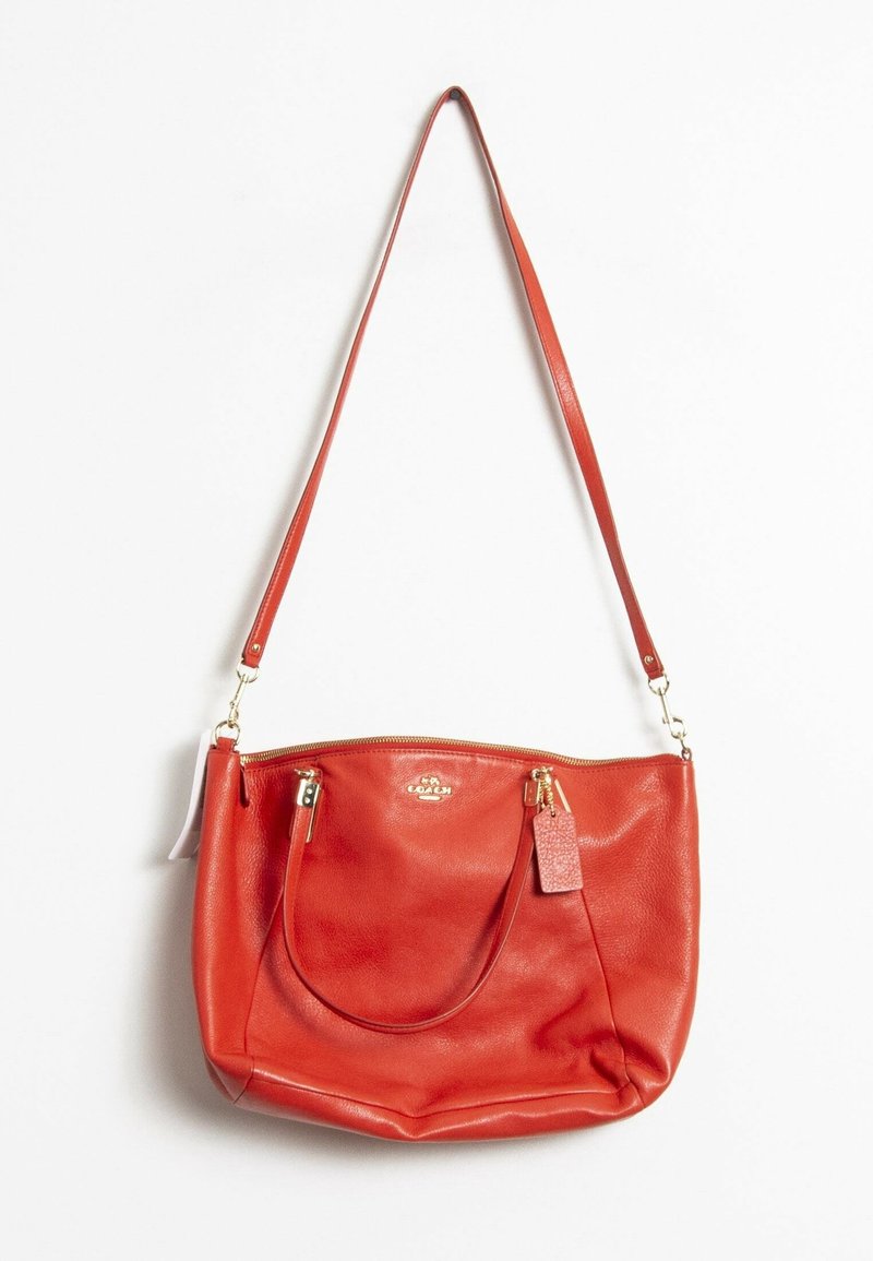 Sac à épaule en cuir rouge avec garnitures dorées, texture lisse, deux bandoulières et fermeture éclair ; comprenant une petite étiquette.