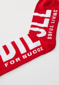 Red crew sock featuring bold white text that reads "WILL FOR SUCCESSFUL LIVING" with alternating ribbed and smooth texture.