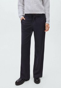 Pantaloni largi cu dungi navy, confecționați dintr-un material texturat, având talie cu șnur elastic și buzunare laterale, asortați cu botoși negri.