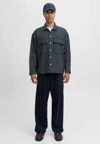 Giacca oversize a scacchi bianco e nero con due tasche sul petto, abbinata a pantaloni a gamba larga blu navy e un cappellino blu scuro.