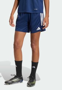 Μπλε ναυτικό αθλητικό σορτς, κατασκευασμένο από αναπνεύσιμο ύφασμα, με λευκές ρίγες στο πλάι και λογότυπο Adidas. Συνδυασμένο με μαύρες κάλτσες και παπούτσια ποδοσφαίρου.