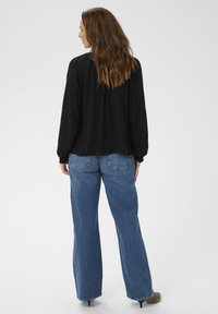 Maglietta nera a maniche lunghe con una vestibilità comoda, abbinata a jeans a gamba larga blu chiaro. I jeans presentano tasche posteriori e una texture sottile.