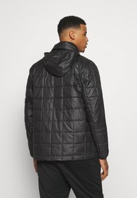 Zwarte geïsoleerde jas met een doorgestikt ontwerp, afneembare capuchon en een gladde textuur. Heeft elastische manchetten en een rechte zoom bij de taille.