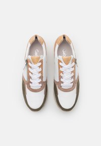 Baskets blanches avec des accents en suède marron et vert, dotées d'une fermeture éclair et d'un design à lacets. Détails perforés sur les côtés.