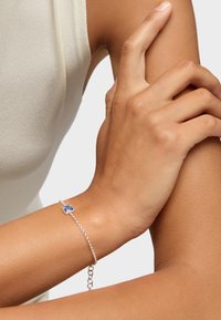 Bracciale in argento con ciondolo a quadrifoglio blu. La catena è delicata, con piccoli anelli tondi e una chiusura regolabile.