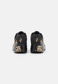 Scarpe sportive nere con una finitura testurizzata, caratterizzate da motivi astratti oro e argento, un tacco imbottito e un design elegante.