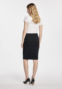 Czarna spódnica ołówkowa o gładkiej fakturze, długości do kolan, w zestawie z dopasowaną białą koszulką i czarnymi szpilkami.