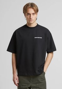 Zwarte korte mouwen t-shirt met witte tekst "PROHIBITED" op de voorkant. Gemaakt van gladde stof met een relaxte pasvorm en ronde hals.