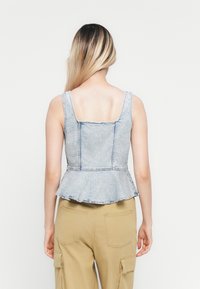 Denim peplum top in een lichte wassing met een vierkante halslijn en stikseldetails. Kenmerkt zich door een uitlopende zoom en brede schouderbanden.