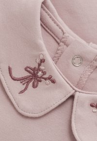 Roze kledingstuk met een zachte textuur, ronde kraag en een verfijnd borduurontwerp van bloemen in donkerroze en crèmekleurige accenten.
