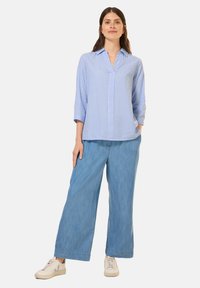 Camicia azzurra a righe con bottoni, maniche a tre quarti, abbinata a pantaloni ampi in denim chiaro e scarpe da ginnastica bianche.