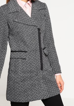 Hondstooth-patroon jas in zwart en wit, met een kruisditemontage, ritsluiting en zijzakken, met een getailleerde pasvorm.