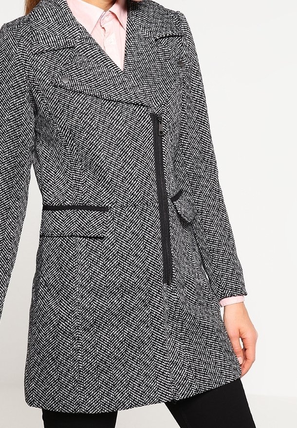 Abrigo de patrón de espiga en blanco y negro, con un diseño cruzado, cierre con cremallera y bolsillos laterales, con un ajuste entallado.