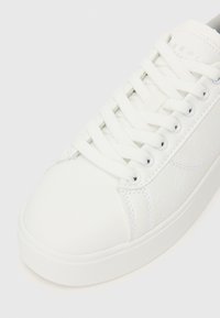 Sneaker bianco con tomaia a texture liscia, lacci tono su tono e dettaglio del logo embossato sul lato. Punta arrotondata e suola piatta in gomma.