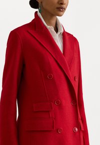 Hănuț roșu din lână, cu dublu voal, cu rever în formă de făltiță, două buzunare frontale și patru nasturi asortați, având o textură fină.